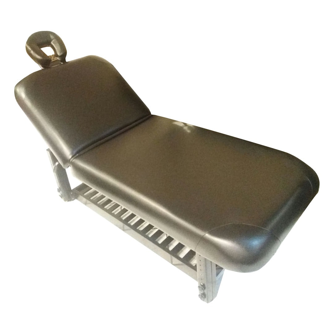 A black salon beauty and facial bed with face cut-out pillow and removable armrests, on a white background.